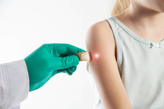 A doctor's hand in a green medical glove peels off a plaster from the shoulder of a girl child after vaccination against measles and rubella. Copy space for text, tuberculosis