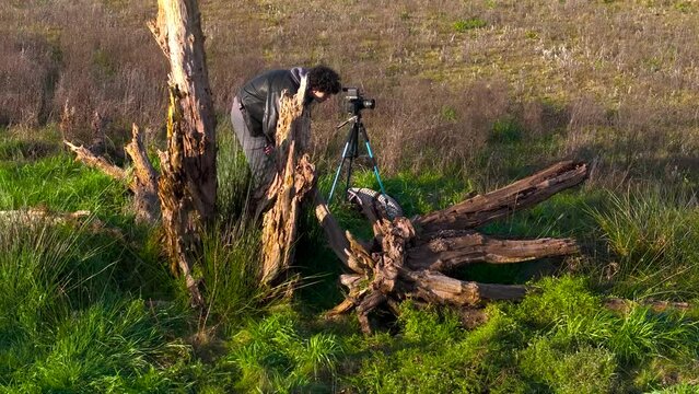 Drone shot of a young Caucasian male photographer checking out his shot on digital camera on tripod