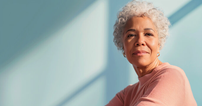 Close up portrait of mature black woman with short gray hair sitting in sunlight, healthy and confident, blue background