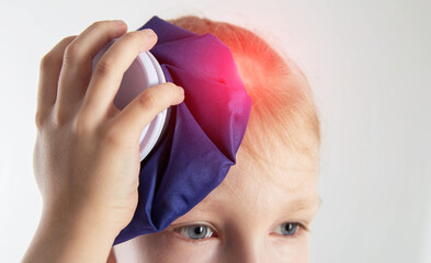 A little girl aged seven holds a cold bag of ice to her head. The concept of applying cold for...