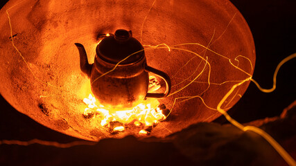 Close up of small metal kettle with hot tea on coals in a fire in Wadi Rum Bedouin Camp at night....