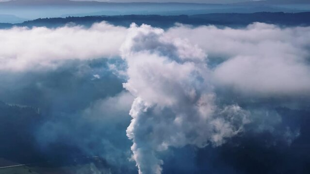 Aerial tilt-down view of white smoke from industrial factory billowing in the atmosphere