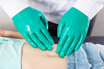 The doctor's hands in green medical gloves probe the child's abdomen in the area of kidney pain....