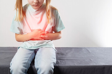 A seven-year-old girl sits and holds her red belly with her hands. Concept of abdominal abdominal pain in children. Enterovirus infection and poisoning. Treatment of abdominal pain in children. 