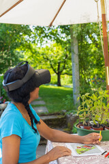 A multiracial woman in VR glasses designs a garden at a table.