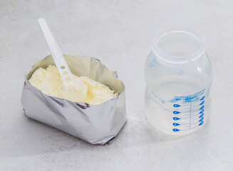 A baby feeding bottle and a measuring spoon with a handful of dry baby formula for preparing milk for the baby. Useful and healthy food, close-up. Baby water bottle