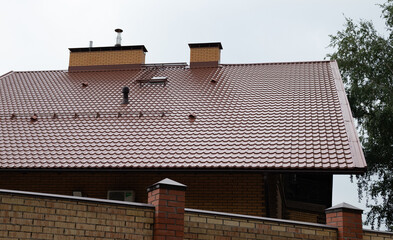 Roof of a new home. Ceramic chimney, metal roof tiles, gutters, roof window. TV antennas attached to the chimney. Single family house.