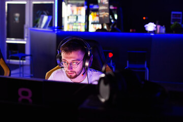 Adult bristly gamer in glasses headset plays video game on PC at computer club cyber sport tournament. Facial expressions. E-sport championship. Multiplayer online tactical shooter real-time strategy