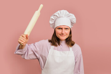 Woman cook threatening to fight on studio pink background. Portrait of a female person in chef's...