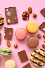 Pastel macarons, almond chocolate, peanut butter cookies and various nuts on bright pink background. Top view.