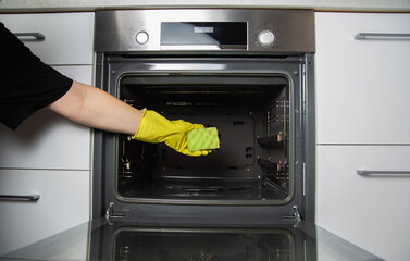 A girl holds a sponge in her hand against the background of an oven. Concept for cleaning electric ovens in the kitchen, cleaning company. Washing up