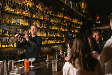 Barman of Ukrainian pub fulfills orders of guests by bar counter. Bartender makes cocktail in front...