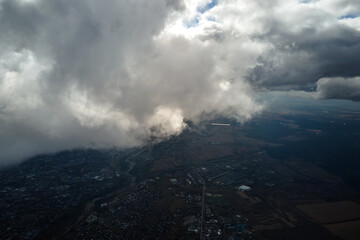 Aerial view from airplane window at high altitude of distant city covered with white puffy cumulus...