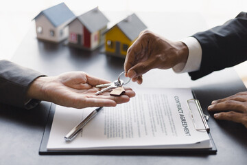 Businessman real estate agent holding house keys is handing them over to a client after signing a...