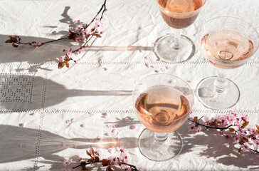 Rose wine in vintage glasses with blooming pink branches, flower petals, romantic mood, spring vibes. Eco linen background, natural spring light, romantic still life  
