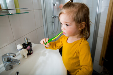 Happy boy with toothbrush standing by bathroom sink. Dental health and hygiene for children. Toddler brushing teeth at home