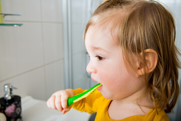 Happy boy with toothbrush standing by bathroom sink. Dental health and hygiene for children. Toddler brushing teeth at home