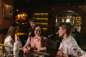 Smiling woman flirts with attractive guy during party in nightclub. Young people meet in fancy bar. Friends with drinks