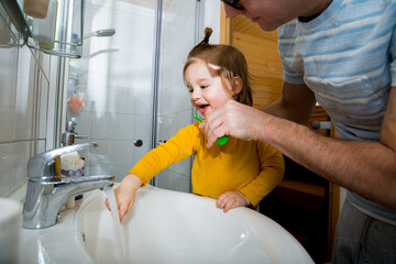 Happy boy and father with toothbrush standing by bathroom sink. Dental health and hygiene for children. Toddler brushing teeth at home. Family life