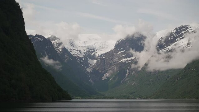 tranquil and calm Oldevatnet glacial lake in front of the melting Briksdalsbren glacier in Norway with snow capped mountains.