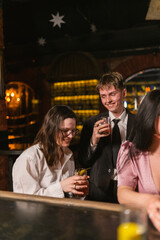Smiling man in formal suit looks at pretty lady in night club. Colleagues reduce work stress drinking cocktails in cozy pub