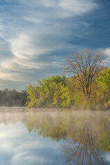 Foggy spring landscape at dawn of the shoreline of Jackson, Hole, Lake with mirrored reflections in calm water, Fort Custer State Park, Michigan, USA