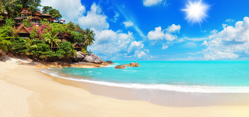 Tropical island paradise sand sea beach, ocean water, palm tree, sun blue sky cloud, villa bungalow on cliff, resort hotel hut houses on rocks, Caribbean, Maldives, Thailand, summer holidays, vacation