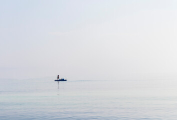 Shot of a man on a small catamaran boat by the horizon, which is hard to detect because of the fog and humidity. Outdoors