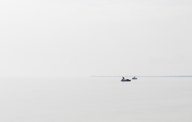 Shot of a man on a small catamaran boat by the horizon, which is hard to detect because of the fog...