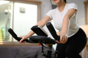Young woman doing cardio workout on stationary bike at home - obrazy, fototapety, plakaty
