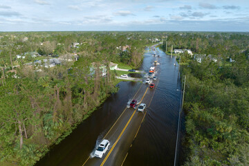 Flooded Florida road with evacuating cars and surrounded with water houses in suburban residential...