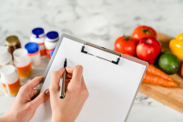 Writing on clipboard with food supplements and vegetables, healthy eating concept. Dietary healthy lifestyle. Dieting for slimming, losing weight. Calories counting