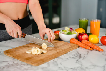 Obraz na płótnie Canvas Nice fit girl cutting banana on cutting board with healthy vegetables and fruits, healthy eating concept. Dieting slimming and losing weight. Zero calories