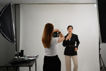 Fashion photographer taking picture of female model with digital camera in lighting studio