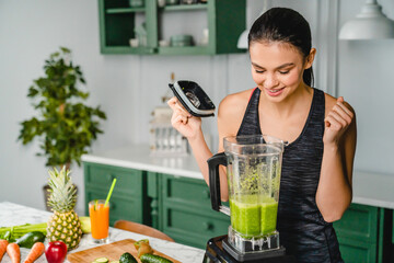 Happy fit girl making fresh detox cocktail in blender in the kitchen for body shaping, slimming....