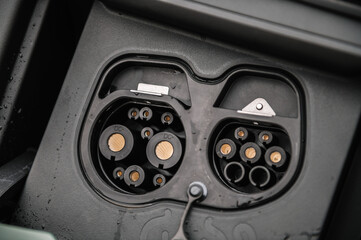 Closeup view of an electric vehicle's charging port with a connector, set against a car body....