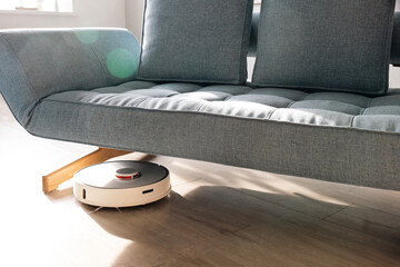 Robot vacuum cleaner on wooden floor under sofa