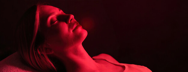 A woman reclines, enjoying red light therapy for wellness or cosmetic treatment. Female appears tranquil under the therapeutic glow, likely seeking rejuvenation or healing.