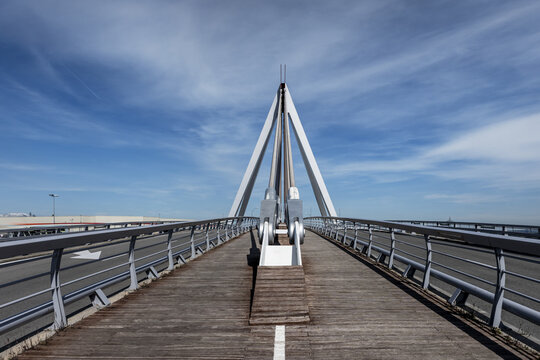 Bridge with wooden pedestrian walkway floor with paint marks and metal braces to support the structure on a day with blue skies