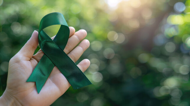 Mental health awareness week background - green ribbon in a hand with bokeh background