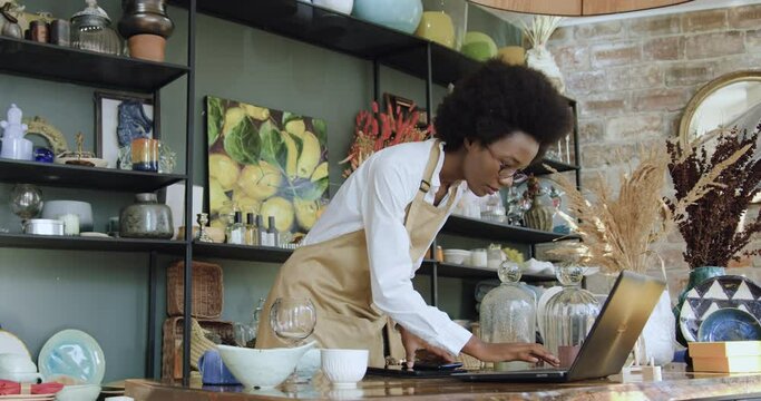 Portrait of african american woman using smartphone and laptop her own shop and uploading photo for internet market. Small family business concept.