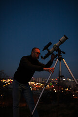 Amateur astronomer looking at the evening skies, observing planets, stars, Moon and other celestial objects with a telescope in urban city area. - obrazy, fototapety, plakaty