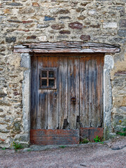 Fototapeta na wymiar Aged wooden door with a small window opening, on an ancient stone wall