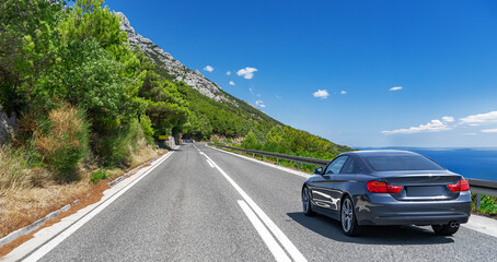 Fototapeta premium Blue car drives along the sea coastline on a sunny summer day.