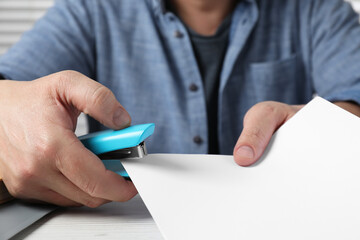 Man with papers using stapler at white table, closeup