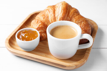 Fresh croissant, jam and coffee on white wooden table, closeup. Tasty breakfast
