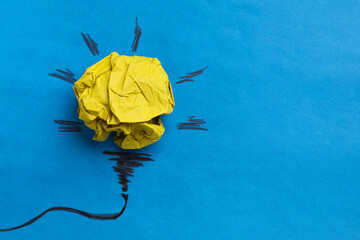 Idea concept. Light bulb made with crumpled paper and drawing on blue background, top view. Space...
