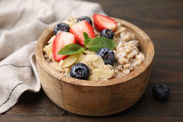 Tasty oatmeal with strawberries, blueberries and almond petals in bowl on wooden table, closeup