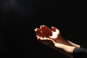 Religion. Woman with open palms praying on black background, closeup. Space for text