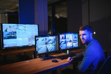 Rear view of security system operator looking at CCTV footage at desk in office